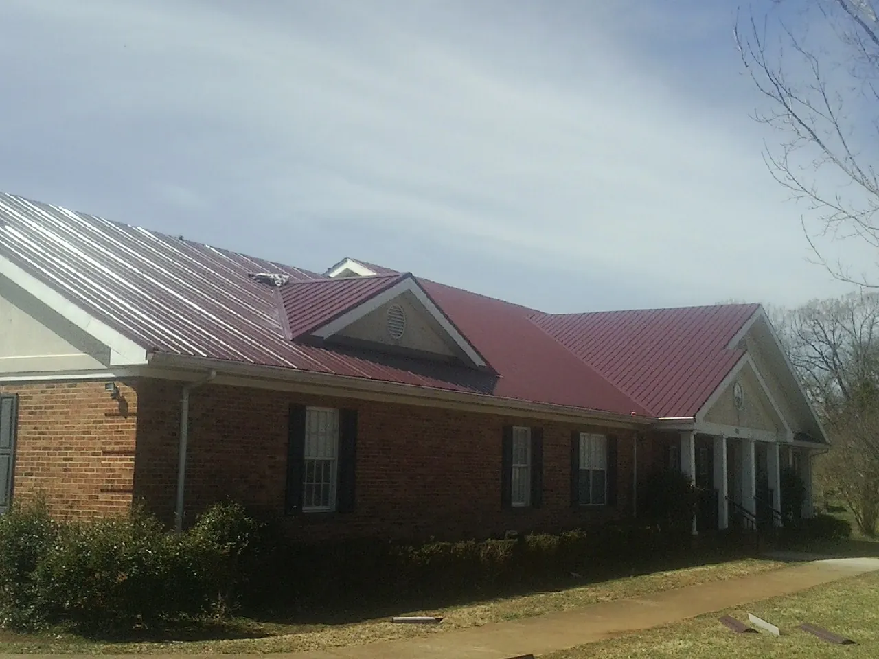 Red metal roof with gabled entries on a long brick building, from a Hail Damage Roof Repair job in Dalzell