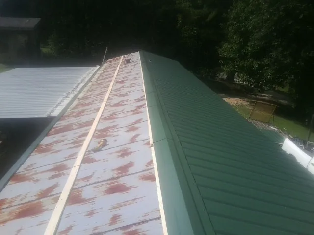 Old rusted panels beside newly installed green metal roofing — Wind Damage Roof Repair by Roofing Brothers in Dalzell