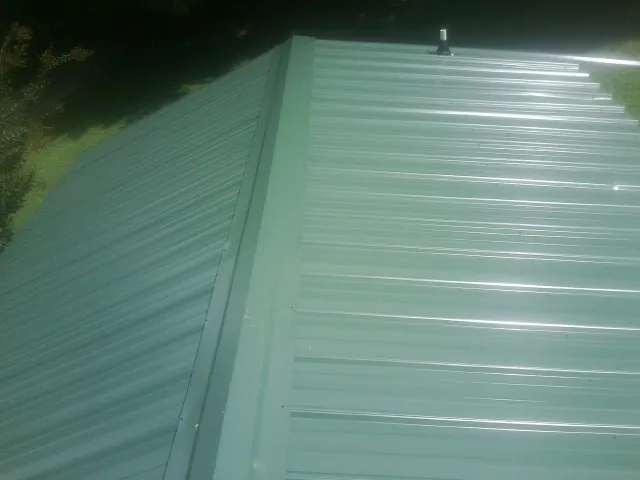 New green metal panels meeting at the ridge of a roof — Flat Roof Repair work by our crew in Dalzell