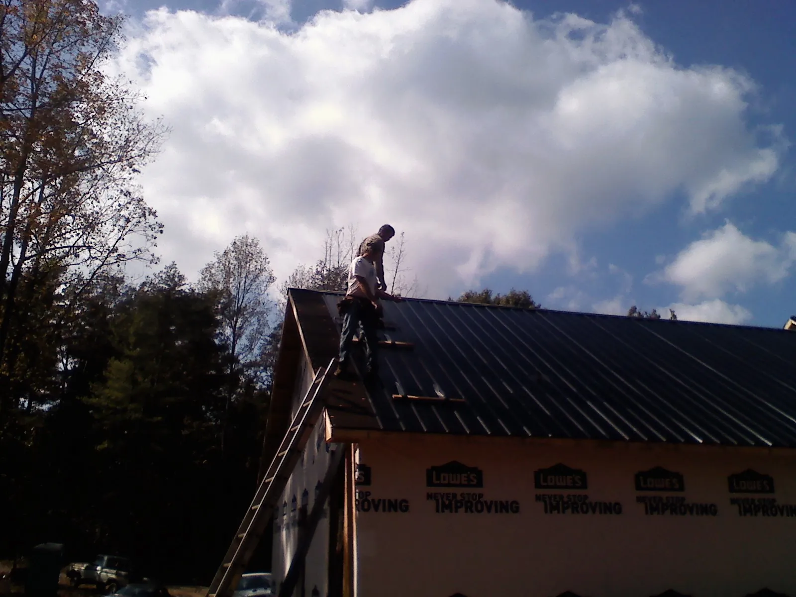 Roofer fastening dark metal panels high against a cloudy sky, from a Roof Inspection job in Dalzell